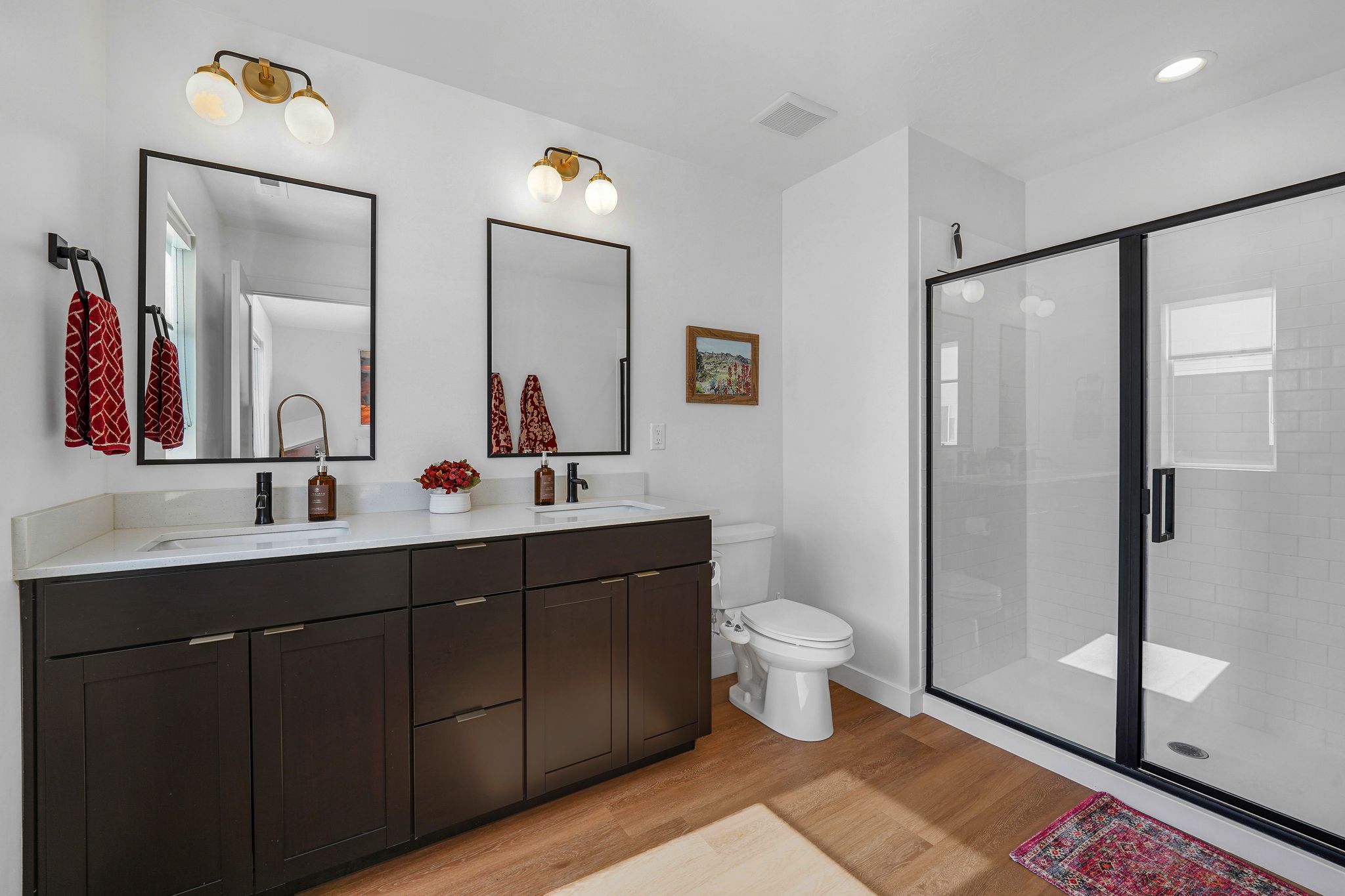 Full bath with double vanity, a stall shower, and light wood finished floors