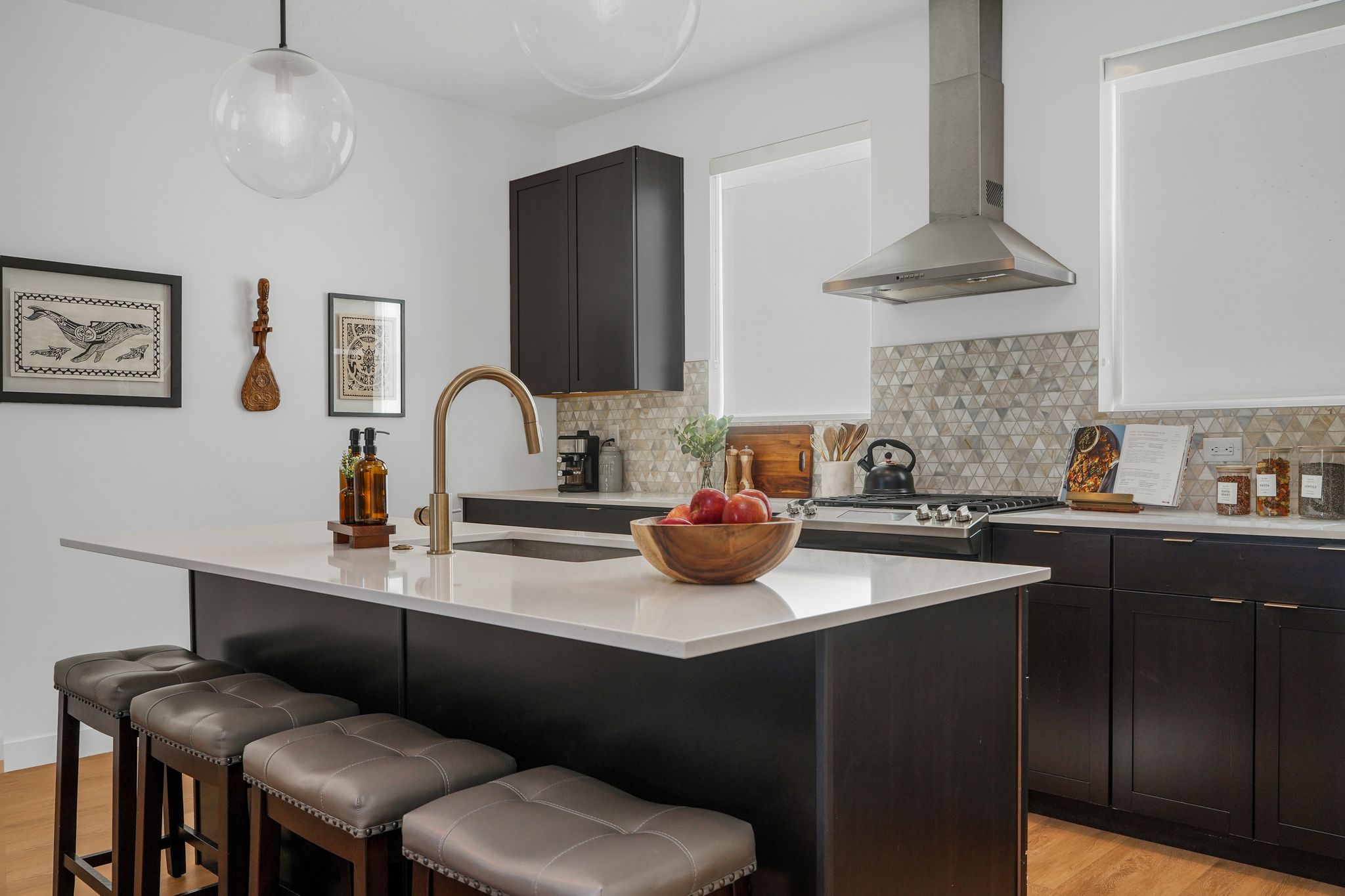Kitchen featuring light wood-style floors, a breakfast bar area, a center island with sink, light stone countertops, and decorative light fixtures