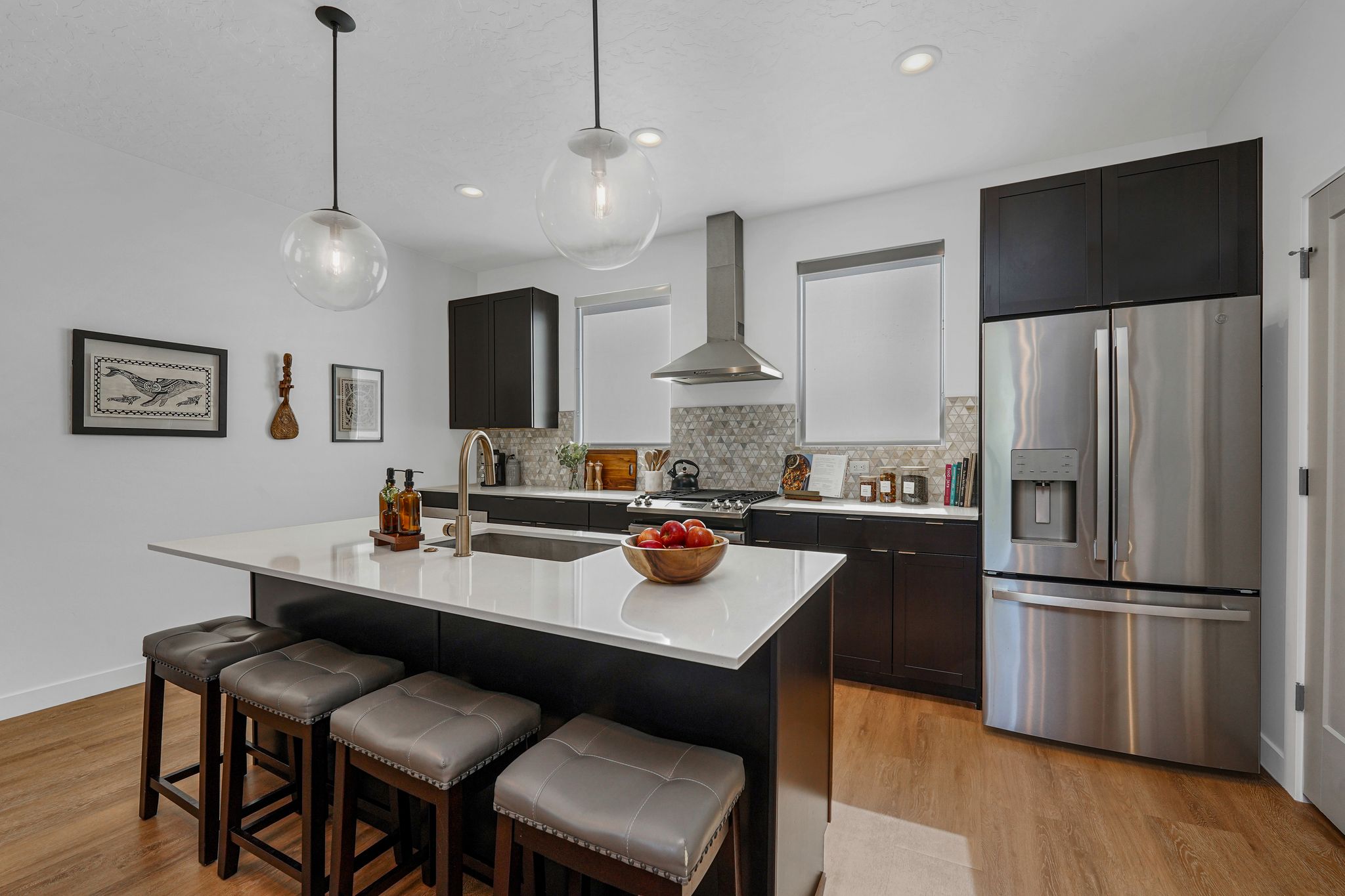 Kitchen featuring stainless steel appliances, decorative light fixtures, light wood-type flooring, dual tone cabinets, and a center island with sink