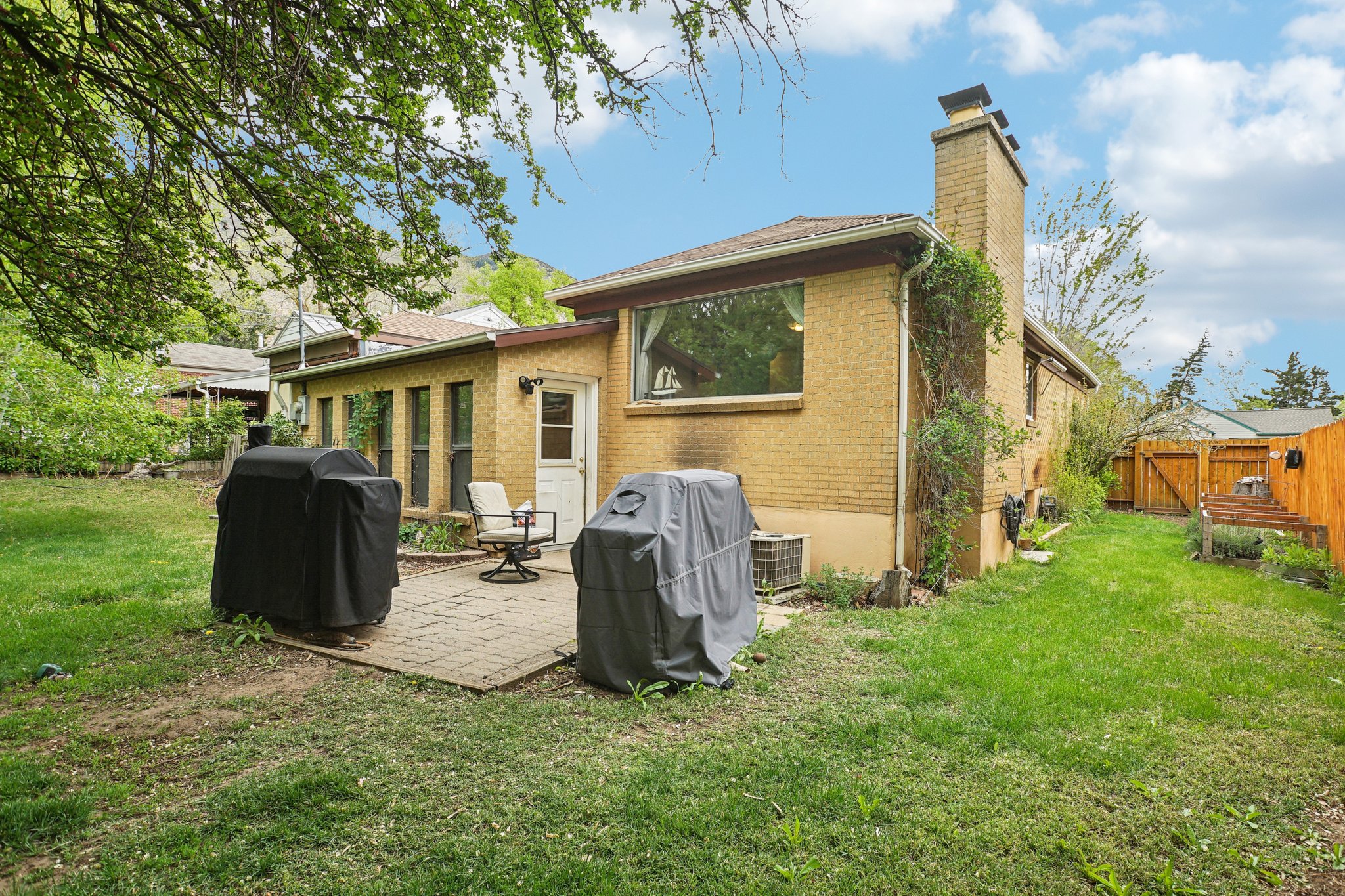Expansive backyard featuring a brick paver patio, a full brick exterior, a prominent brick chimney, and a wooden fence