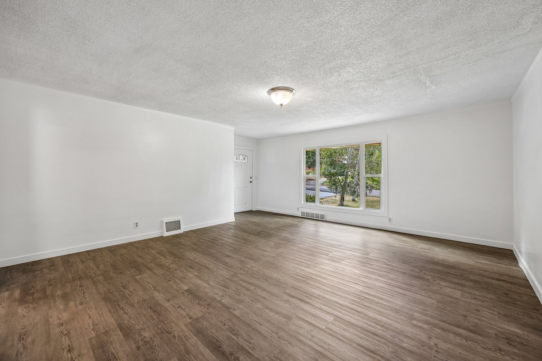 Spacious interior featuring wood-finish flooring, white walls, and a large front-facing window