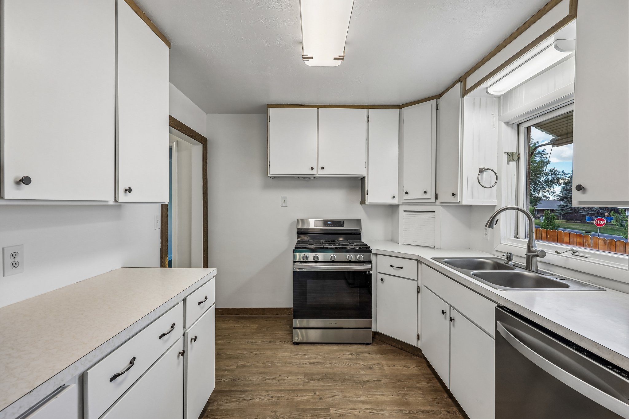 Bright kitchen featuring white cabinetry, light countertops, wood-finish flooring, a stainless steel range, and a dual-basin sink with a window