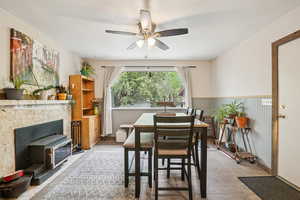 Dining room with wainscoting, wood finished floors, a wood stove, and a ceiling fan