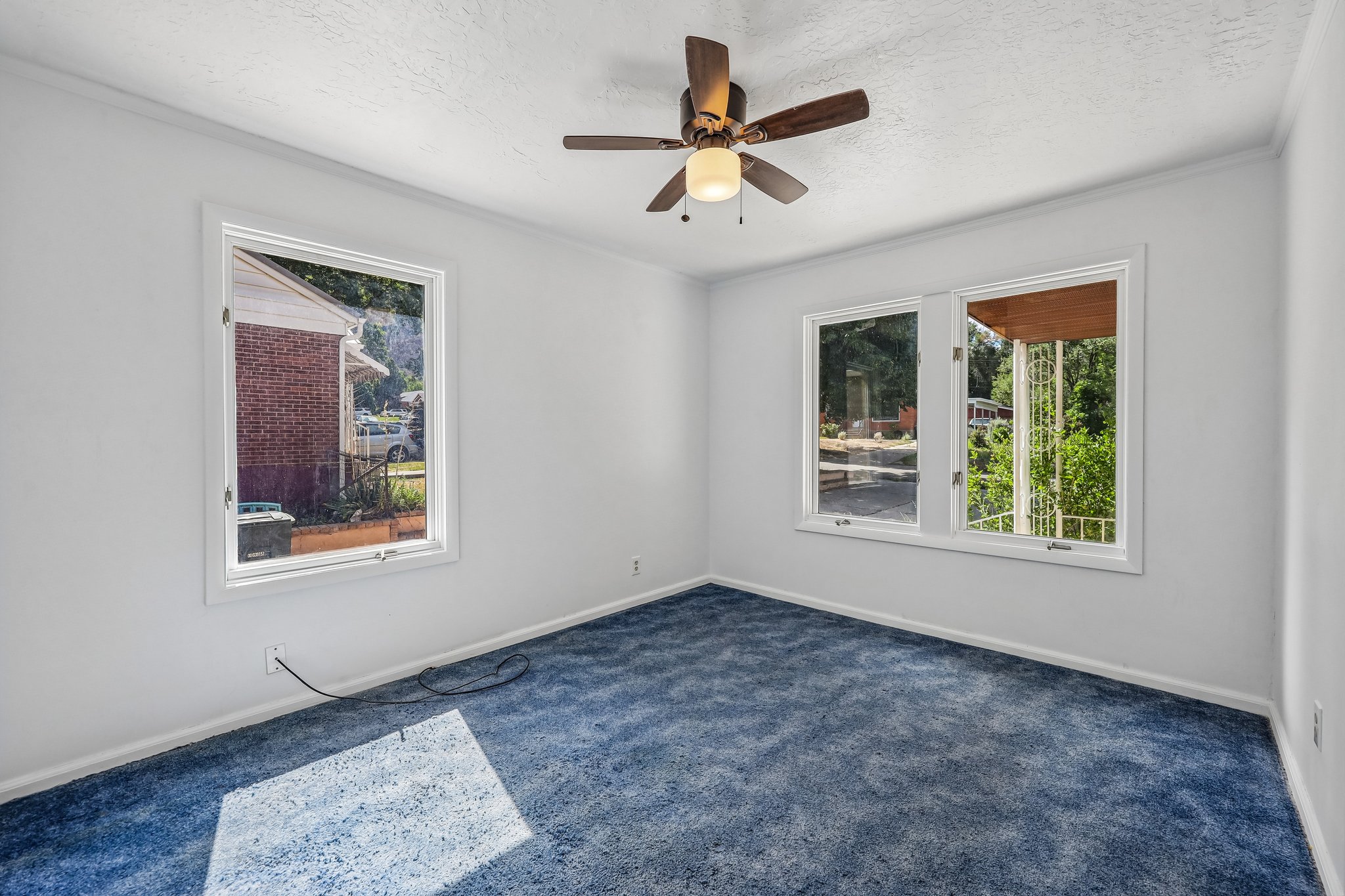 Spacious room featuring blue carpeting, white walls, multiple windows, a ceiling fan with integrated lighting, and white baseboards