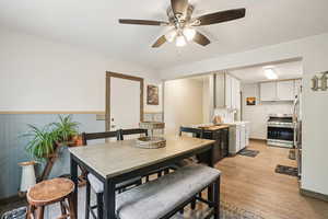 Dining room featuring light wood-style flooring, ceiling fan, and a wainscoted wall