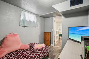 Bedroom featuring a textured wall, a textured ceiling, and wood finished floors