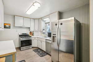 Kitchen featuring stainless steel appliances, light countertops, white cabinetry, a textured ceiling, and light wood-style flooring