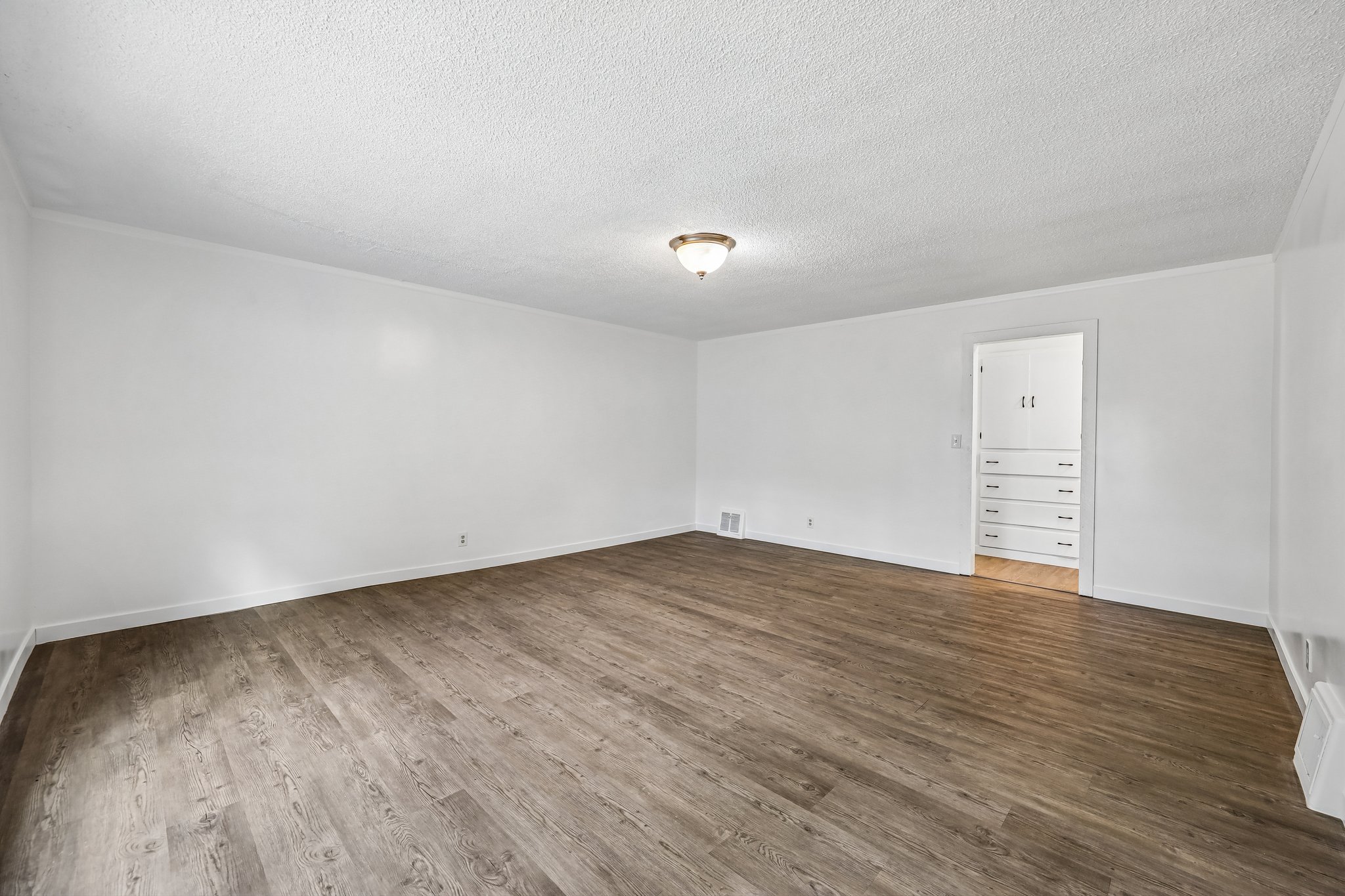 Spacious interior room featuring wood-finish flooring, white walls, and a textured ceiling with a flush-mount light fixture