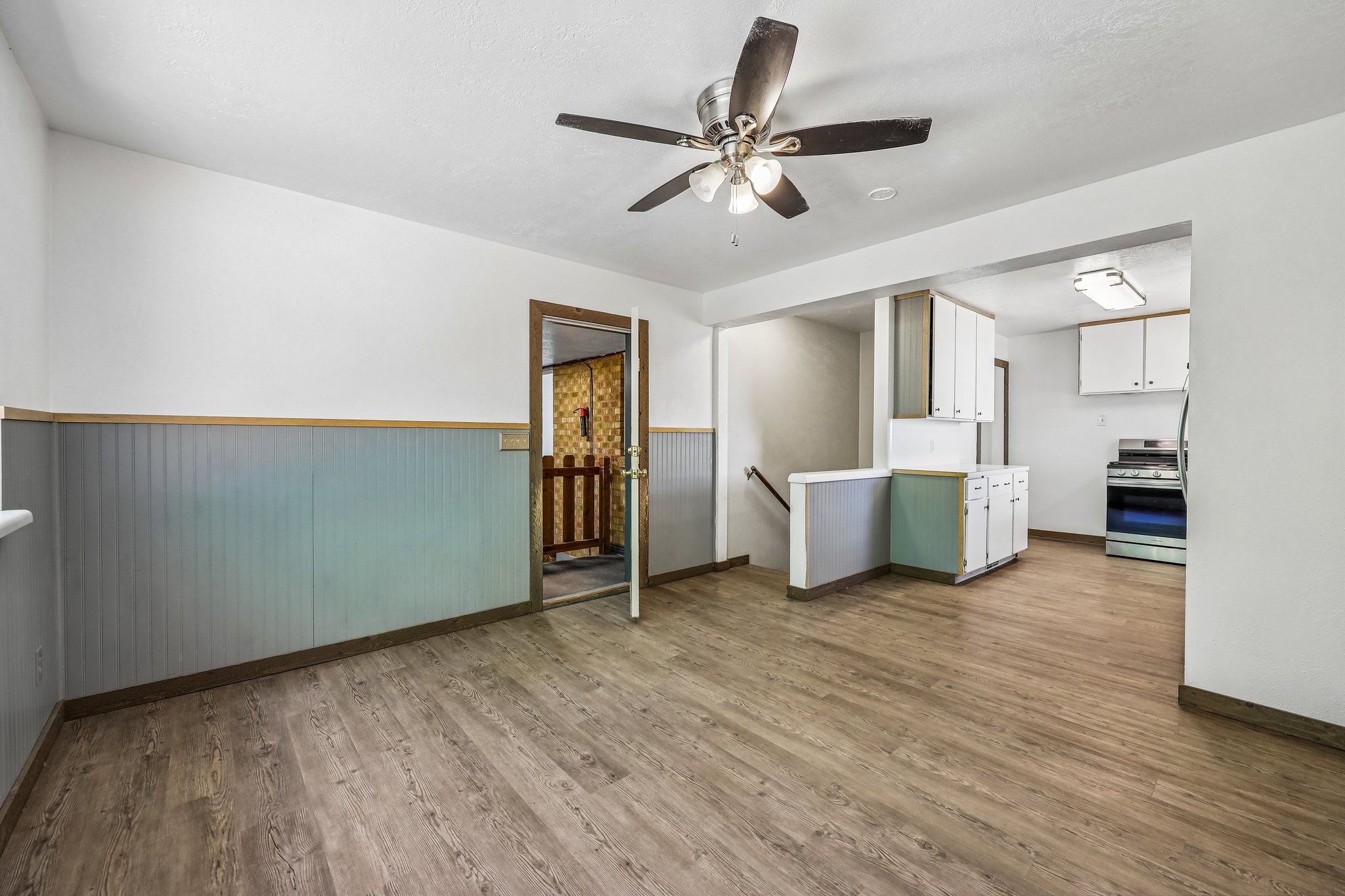 Open-concept living area featuring wood-finish flooring, a ceiling fan with integrated lighting, and a defined kitchen space