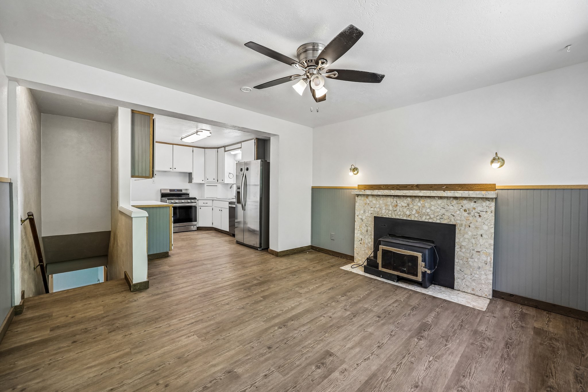 Open-concept living area featuring wood-finish flooring, a ceiling fan, and a fireplace with a stone surround