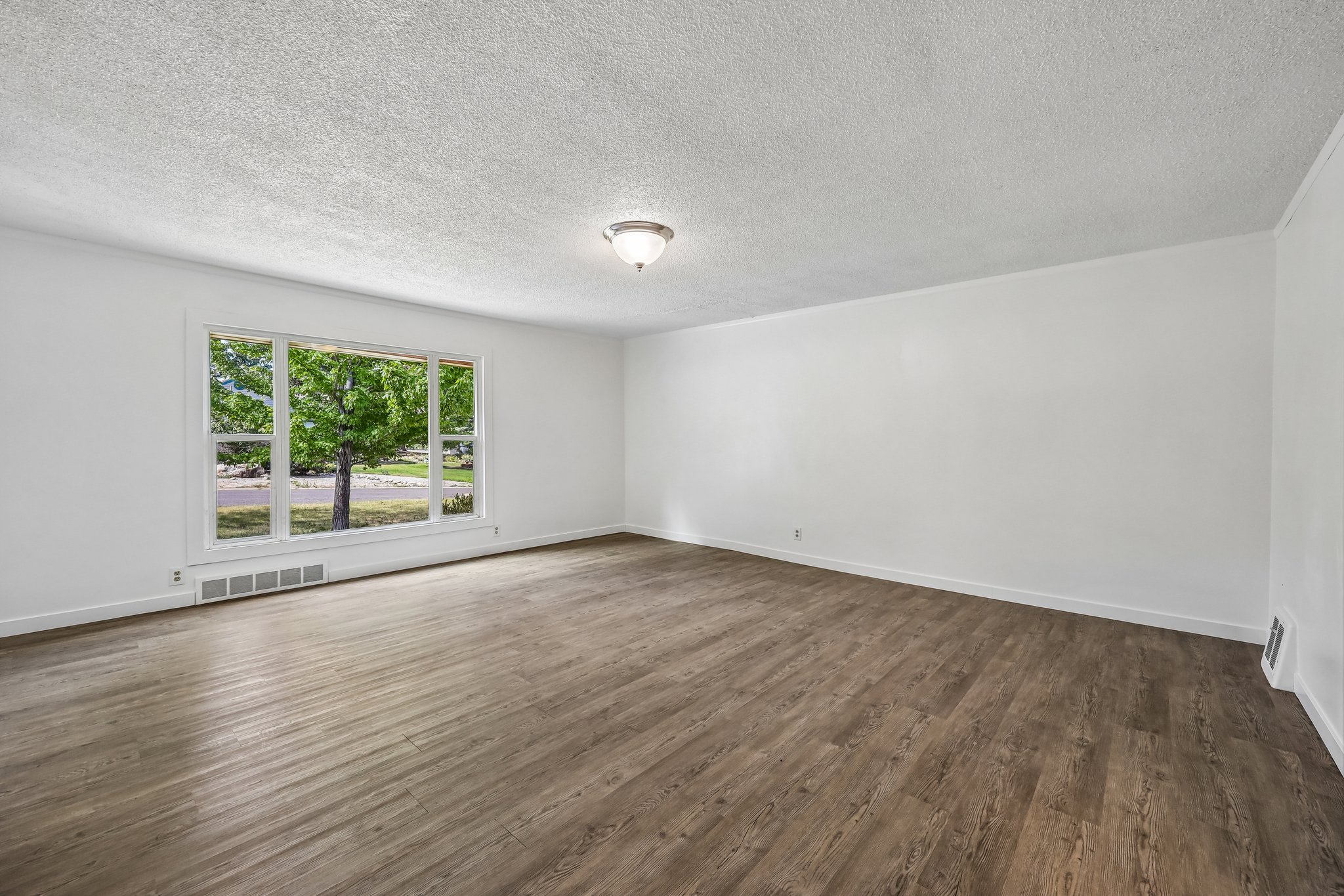 Spacious room featuring wood-finish flooring, white baseboards, and bright white walls