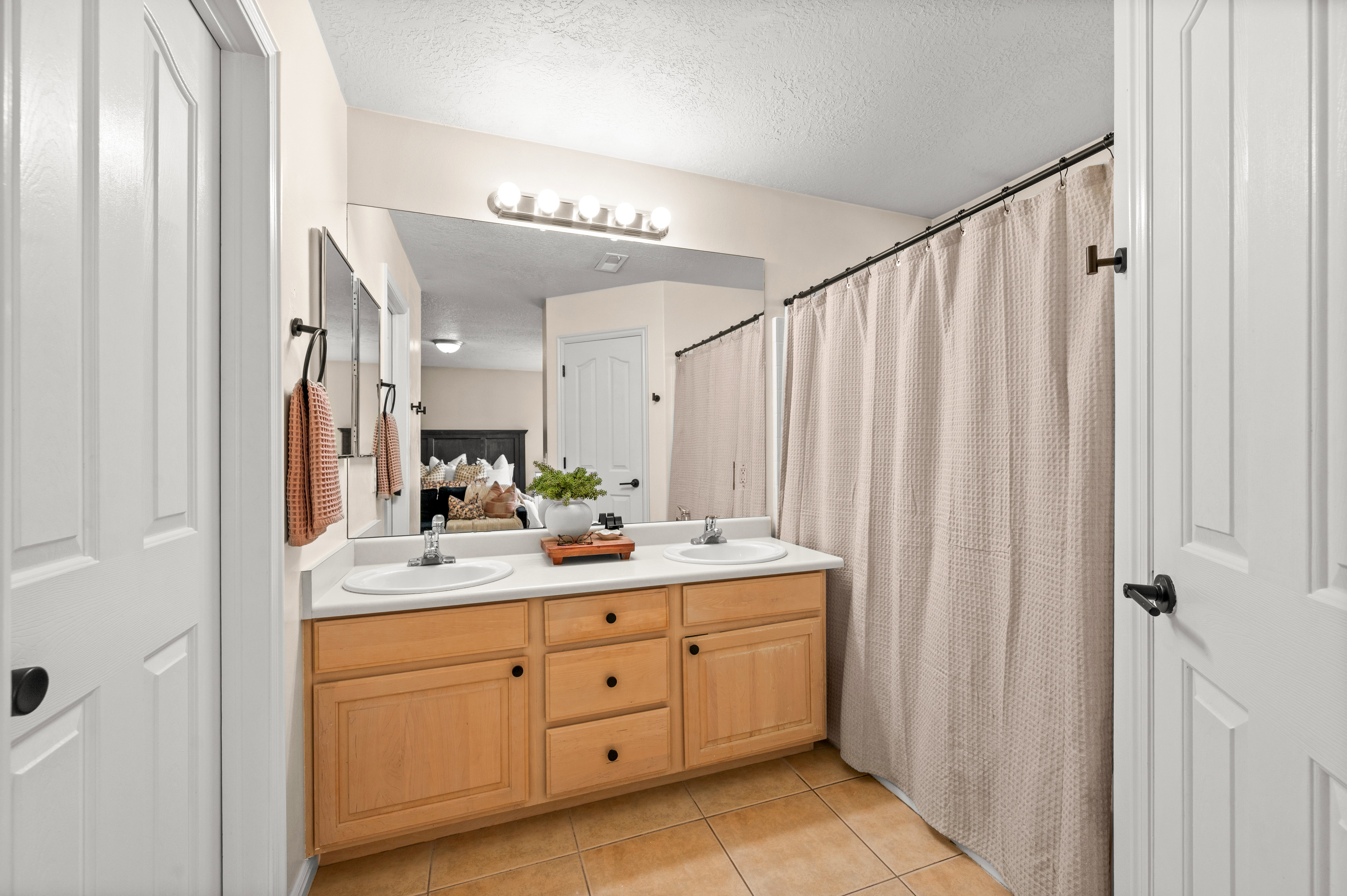Bathroom with double vanity, light tile patterned floors, curtained shower, and a textured ceiling
