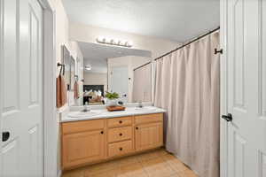 Bathroom with double vanity, light tile patterned floors, curtained shower, and a textured ceiling