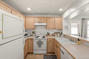 Kitchen featuring white appliances, light wood finish cabinets, light countertops, a peninsula, and recessed lighting