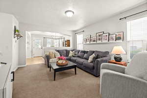 Living room featuring arched walkways, a textured ceiling, light colored carpet, and a chandelier