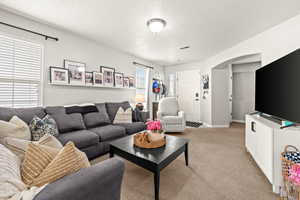 Living room featuring arched walkways, light carpet, and a textured ceiling