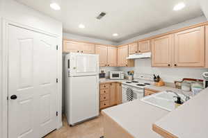 Kitchen with white appliances, light wood finish cabinets, light countertops, light tile patterned floors, and recessed lighting