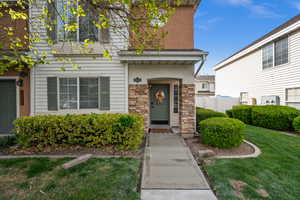 Entrance to property with stone siding, a lawn, and stucco siding