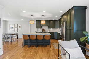 Kitchen with hanging light fixtures, light stone countertops, a kitchen island with sink, freestanding refrigerator, and a kitchen breakfast bar