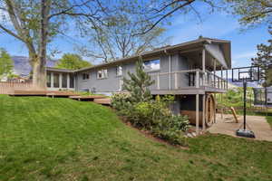 Back of property with a trampoline, a deck, a lawn, and brick siding