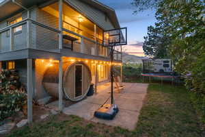 Back of house at dusk featuring a trampoline, a balcony, a patio, and a yard