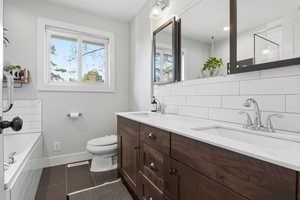 Bathroom with backsplash, double vanity, dark tile patterned flooring, a garden tub, and a shower