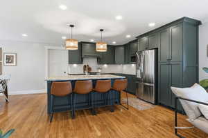 Kitchen with light stone counters, stainless steel fridge with ice dispenser, a kitchen island with sink, a kitchen bar, and hanging light fixtures