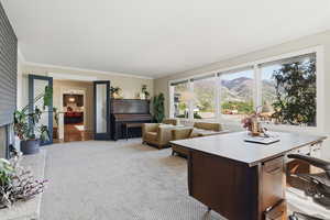Living area with a mountain view, light carpet, a fireplace, crown molding, and a desk