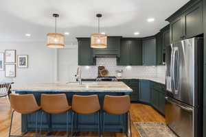 Kitchen with stainless steel appliances, light stone countertops, green cabinetry, a kitchen bar, and tasteful backsplash