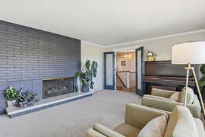 Living area featuring a brick fireplace, carpet floors, ornamental molding, and a chandelier