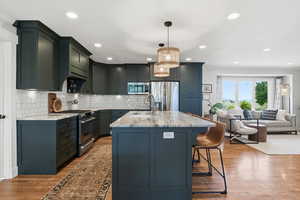 Kitchen with light stone countertops, stainless steel appliances, dark wood-style floors, open floor plan, and hanging light fixtures