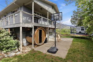 Back of house with a trampoline, a balcony, a lawn, a mountain view, and a patio area