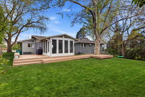 Back of house with a wooden deck, a sunroom, a chimney, and a yard