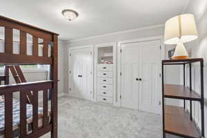 Bedroom with multiple closets, ornamental molding, and light carpet