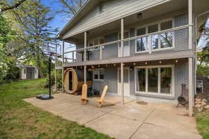 Back of house with a balcony, brick siding, a lawn, and a patio area