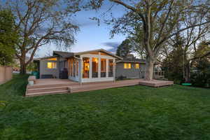 Rear view of property with a wooden deck, a sunroom, board and batten siding, and a yard