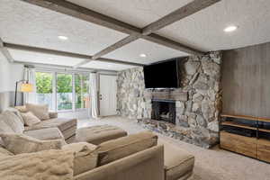 Carpeted living room featuring wooden walls, beamed ceiling, a stone fireplace, recessed lighting, and a textured ceiling