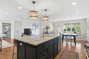 Kitchen with open floor plan, light stone counters, a kitchen island with sink, light wood-style floors, and ornamental molding