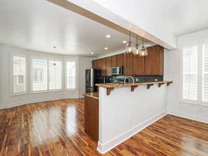 Kitchen featuring dark stone countertops, a peninsula, a kitchen breakfast bar, decorative backsplash, and dark wood finished floors