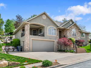 View of front facade featuring stucco siding, stone siding, a balcony, and an attached garage