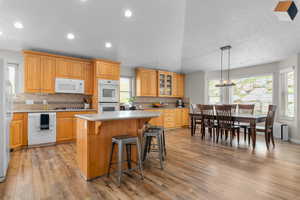 Kitchen featuring breakfast bar, island, light countertops, white appliances, and light wood-style flooring