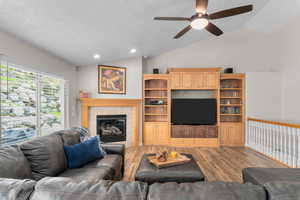 Living room featuring lofted ceiling, wood finished floors, a ceiling fan, recessed lighting, and a tiled fireplace