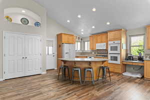 Kitchen featuring a breakfast bar, a center island, white appliances, vaulted ceiling, and light wood-style flooring