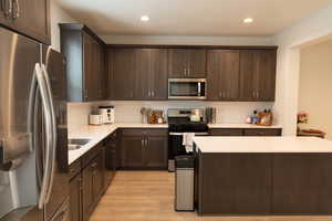 Kitchen featuring dark wood finish cabinetry, stainless steel appliances, light wood-style flooring, a kitchen island, and recessed lighting