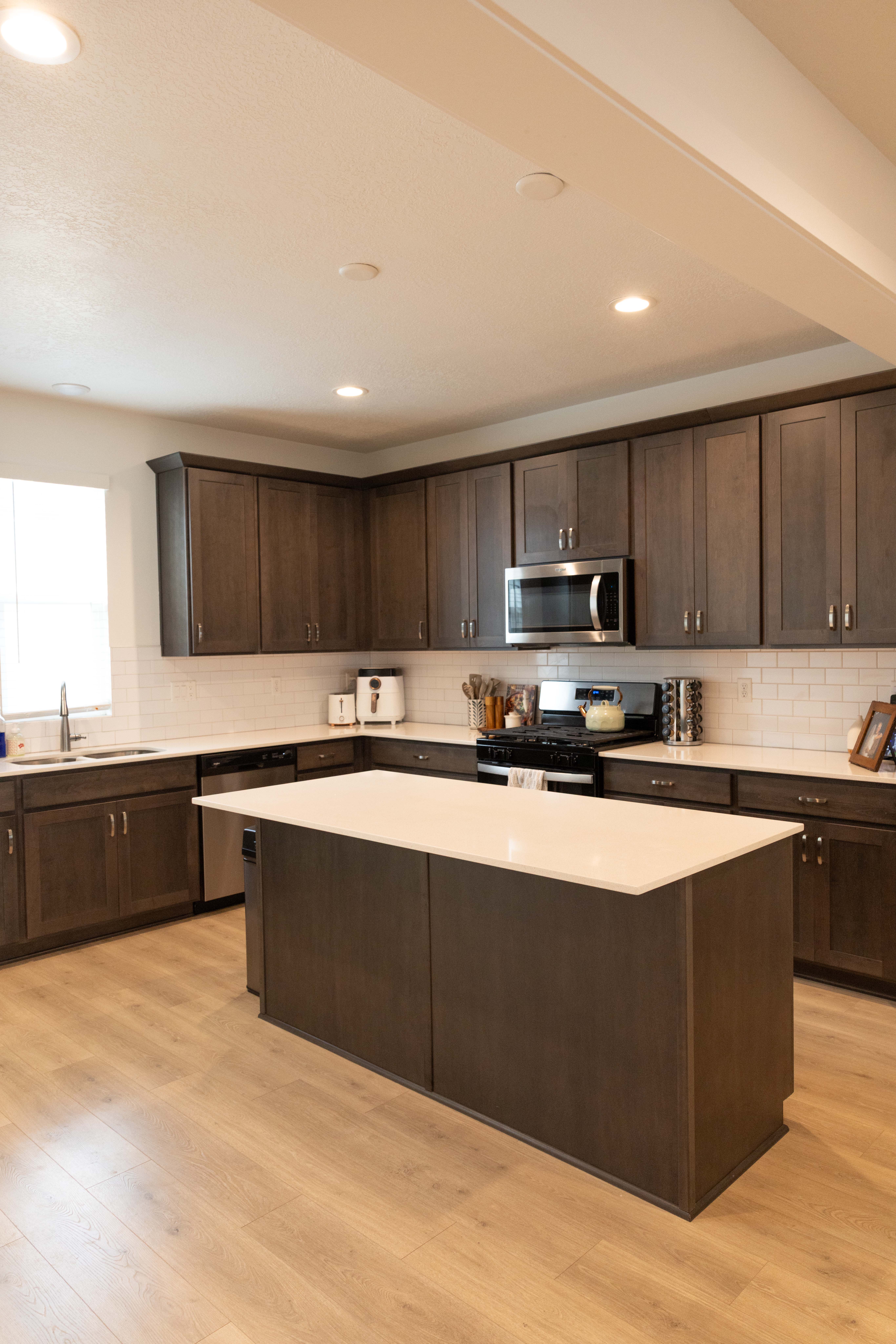 Kitchen with dark wood finish cabinets, a kitchen island, stainless steel appliances, light wood-style floors, and tasteful backsplash