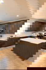 Kitchen with dark wood finish cabinets, a kitchen island, stainless steel appliances, light wood-style floors, and tasteful backsplash