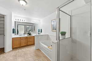 Full bath with vanity, a stall shower, a garden tub, and a textured ceiling