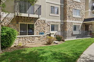 Back of house with a balcony, stone siding, a lawn, and stucco siding
