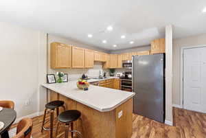 Kitchen featuring stainless steel appliances, light wood-style floors, light countertops, light wood finish cabinets, and a peninsula
