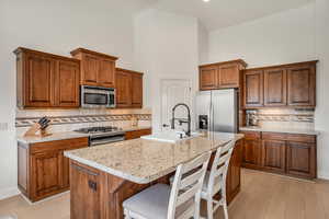 Kitchen featuring wood finish cabinetry, light stone counters, stainless steel appliances, and a high ceiling